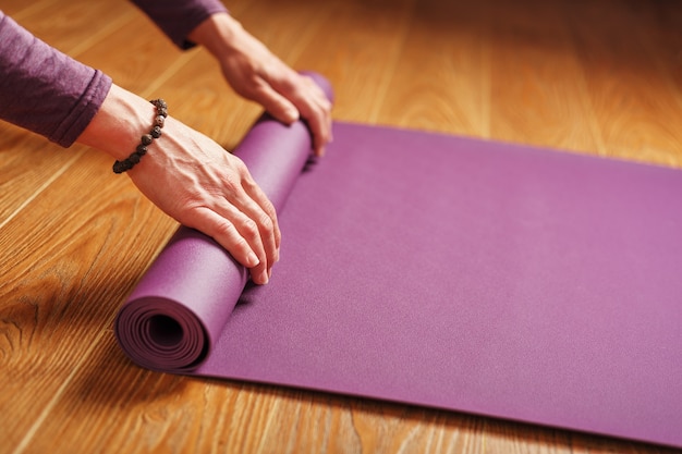 le mani di una donna piegano un tappetino da yoga o fitness lilla dopo un allenamento a casa