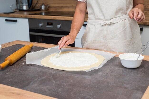 Le mani di una donna stanno spalmando crema di formaggio sulla pasta Preparazione della pizza