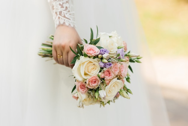 Le mani di una giovane sposa tengono in mano un bellissimo bouquet da sposa delicato. La mano della sposa con un anello nuziale al dito. Sposa in abito bianco