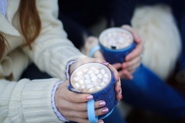 Le mani di una ragazza e un ragazzo tengono tazze con marshmallow al cacao