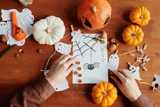 Le mani di una ragazza irriconoscibile che mette piccole decorazioni su una cartolina di Halloween