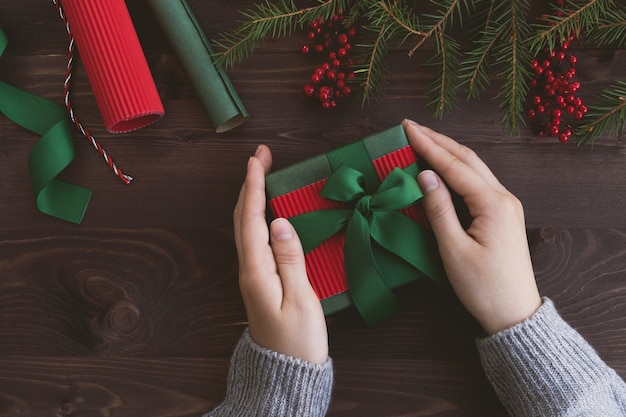 Le mani di Womans tengono il contenitore di regalo di Natale con l'arco sulla tavola di legno