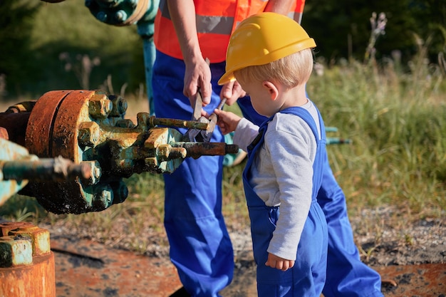 Le mani e il ragazzino del lavoratore adulto in uniforme da lavoro con la chiave a tubo