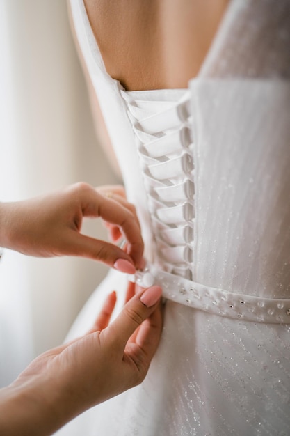 Le mani femminili allacciano una cintura su un abito da sposa sul retro con allacciatura