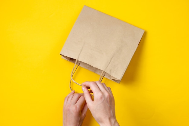 Le mani femminili aprono il sacchetto di carta su un giallo. Vista dall'alto