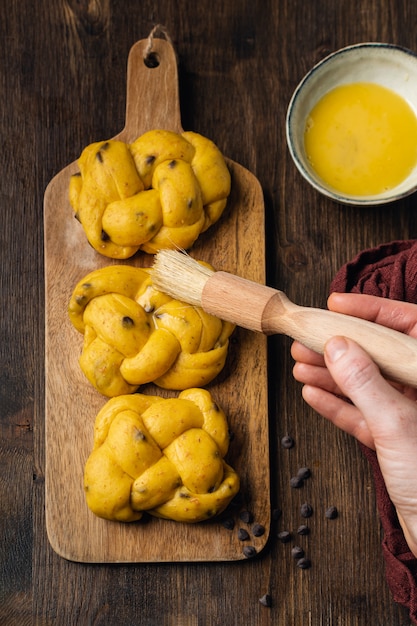 Le mani femminili che fanno l'uovo lavano sulla brioche con le gocce di cioccolato