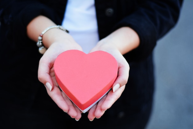 Le mani femminili che tengono il cuore hanno modellato il contenitore di regalo.