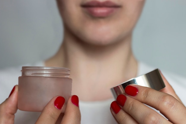 Le mani femminili con il manicure rosso tengono un barattolo aperto con crema. Il concetto di cura del viso. Messa a fuoco selettiva