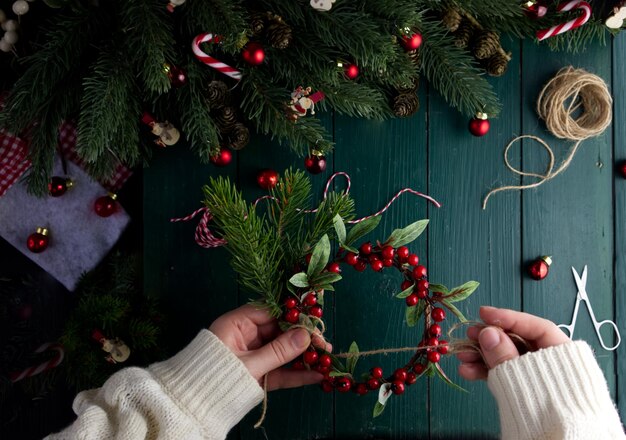 Le mani femminili del primo piano decorano una corona di Natale su un tavolo di legno verde in un decoro di Natale