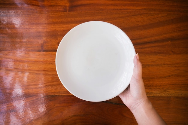 Le mani femminili (donna) tengono (supporto) un piatto bianco (piastra) sul tavolo di legno.