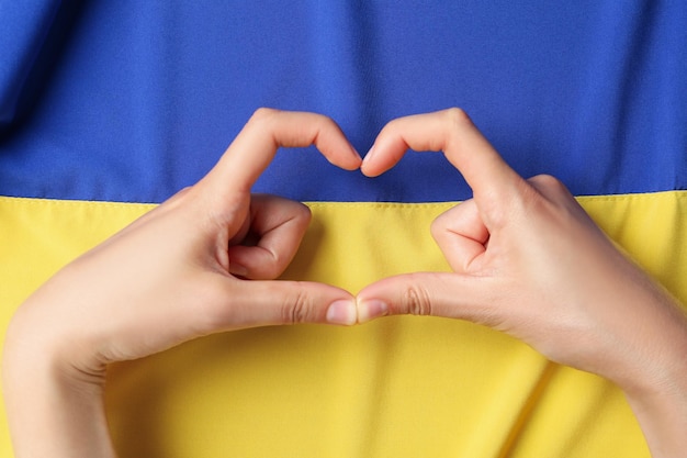 Le mani femminili fanno a forma di cuore sullo sfondo della bandiera ucraina