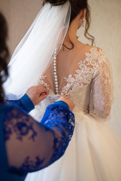 Le mani femminili fissano un pulsante su un abito da sposa la mattina della sposa prima della cerimonia