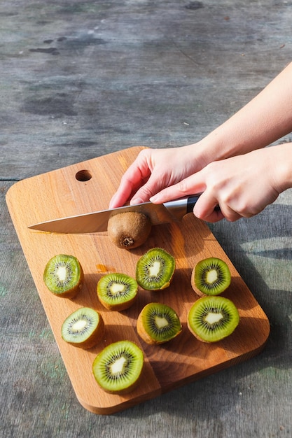 Le mani femminili hanno tagliato il kiwi su un tagliere su fondo d&#39;annata grigio