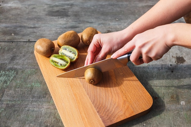 Le mani femminili hanno tagliato il kiwi su un tagliere su fondo d&#39;annata grigio