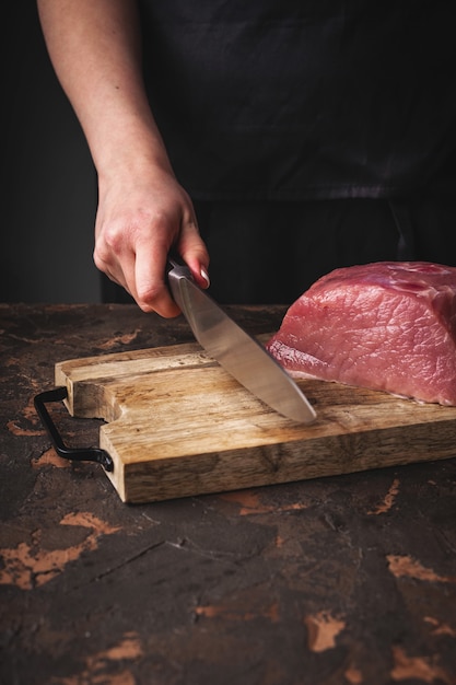 Le mani femminili hanno tagliato la carne di maiale cruda su un bordo di legno nella cucina