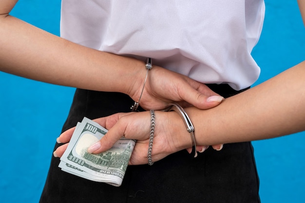 Le mani femminili in manette tengono i dollari isolati sull'azzurro. Prigioniero o arrestato