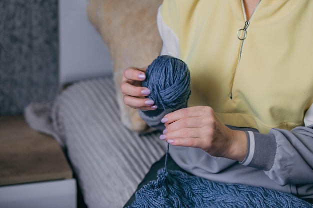 le mani femminili in primo piano tengono in mano un gomitolo di lana e dipanano un vecchio prodotto a maglia