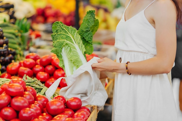 Le mani femminili mettono frutta e verdura in un sacchetto di cotone al mercato alimentare. Borsa ecologica riutilizzabile per lo shopping. Rifiuti zero concetto.