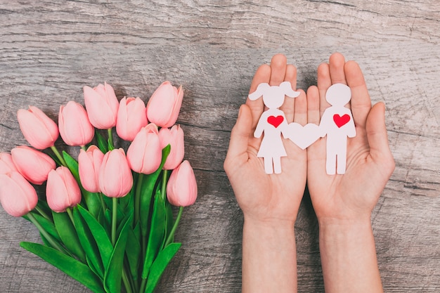 Le mani femminili mostrano due persone di carta, un uomo e una donna, su uno sfondo di legno. San Valentino