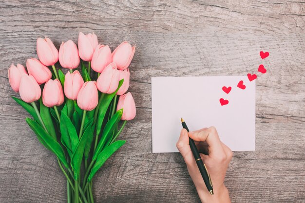 Le mani femminili scrivono un messaggio d'amore su una busta bianca, su uno sfondo di legno. San Valentino