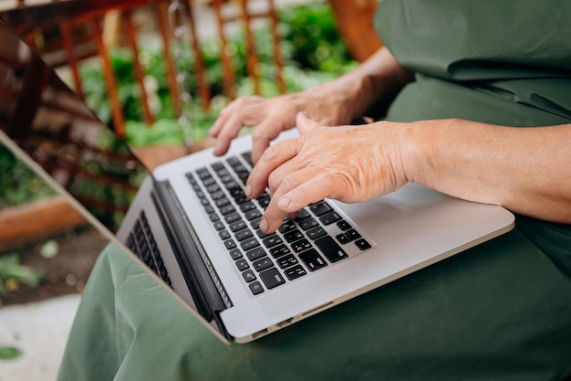 Le mani femminili senior digitano il testo sulla tastiera del laptop