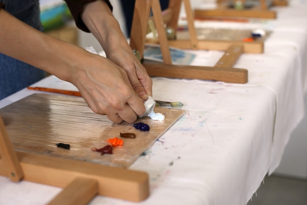 Le mani femminili spremono la pittura a olio bianca su una tavolozza di legno Preparativi per l'officina d'arte