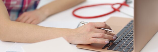 Le mani femminili stanno lavorando al computer portatile accanto allo stetoscopio.