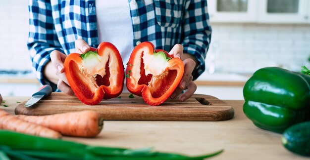 Le mani femminili stanno tagliando i peperoni per l'insalata sul tavolo in cucina