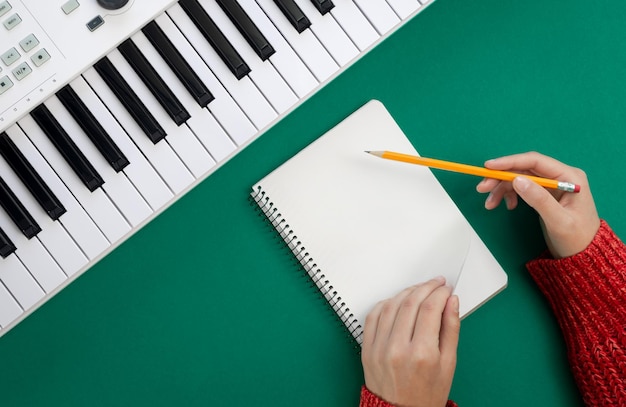Le mani femminili svuotano il blocco note e i tasti musicali su sfondo verde vista dall'alto concetto di creatività musicale