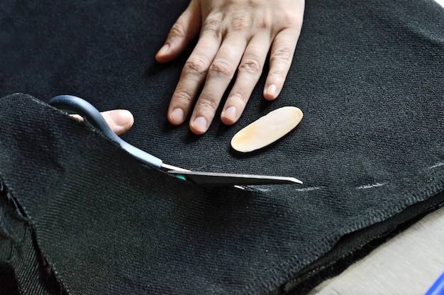 Le mani femminili tagliano il tessuto nero con le forbici. avvicinamento.