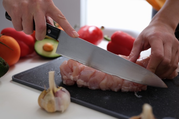 Le mani femminili tagliano la carne con un coltello le verdure sul tavolo