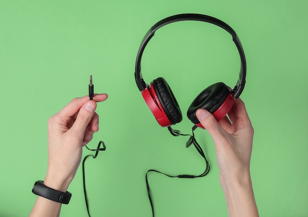 Le mani femminili tengono eleganti cuffie cablate su sfondo verde pastello. Appassionato di musica, DJ. Vista dall'alto.