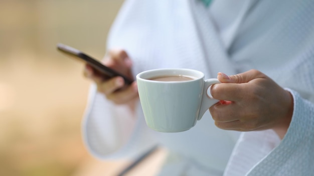 Le mani femminili tengono il caffè in tazza e il telefono cellulare a casa primo piano