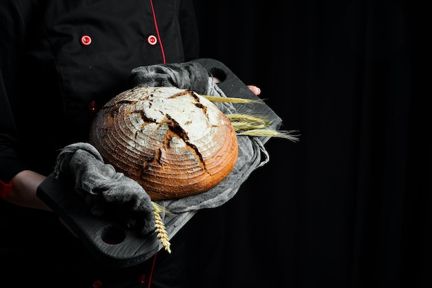 Le mani femminili tengono il pane al lievito fresco su uno sfondo nero