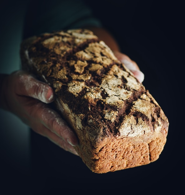 Le mani femminili tengono il pane di segale scuro. Baker con pane fresco al buio