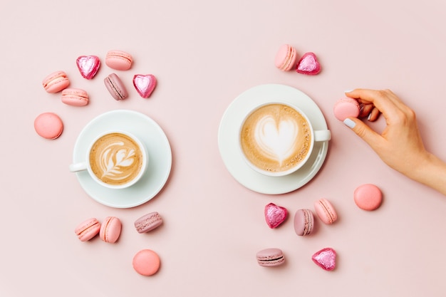 Le mani femminili tengono l'arte del cappuccino su sfondo rosa pallido