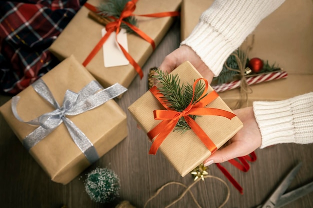 Le mani femminili tengono la scatola regalo con il nastro rosso e il ramo dell'albero di Natale sullo sfondo della decorazione natalizia Il concetto di preparare i regali per le vacanze