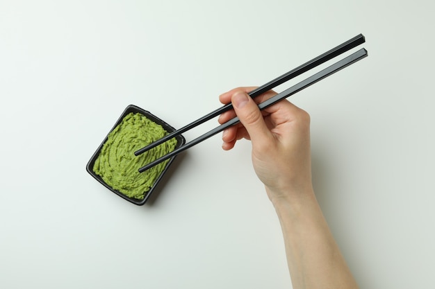 Le mani femminili tengono le bacchette su fondo bianco con la ciotola di wasabi