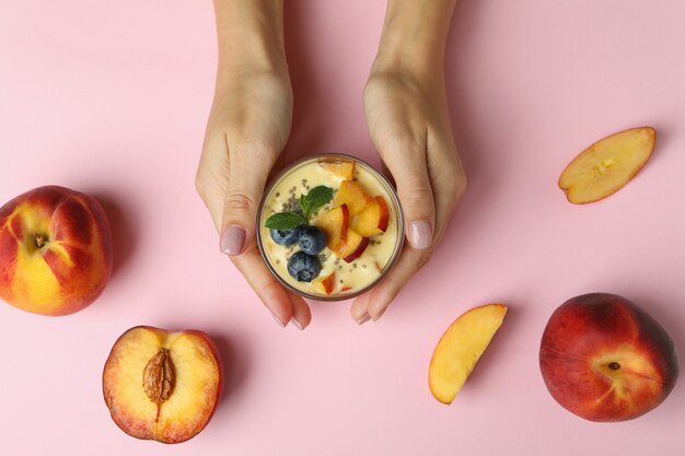 Le mani femminili tengono lo yogurt alla pesca su sfondo rosa