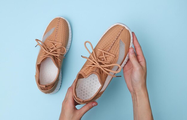 Le mani femminili tengono scarpe sportive alla moda su sfondo blu. Vista dall'alto