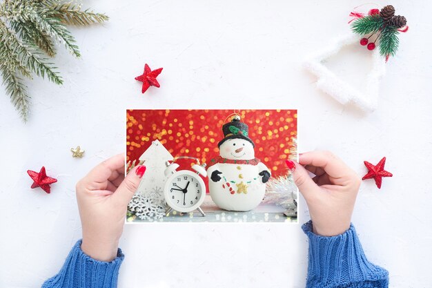 Le mani femminili tengono un biglietto di auguri di Natale sullo sfondo di un tavolo bianco con decorazioni natalizie.