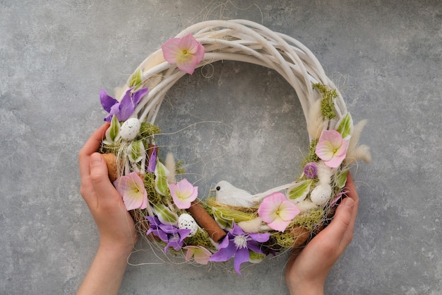 Le mani femminili tengono una corona di Pasqua con fiori e un uccello su un tavolo grigio. Concetto di primavera decorazione della casa.