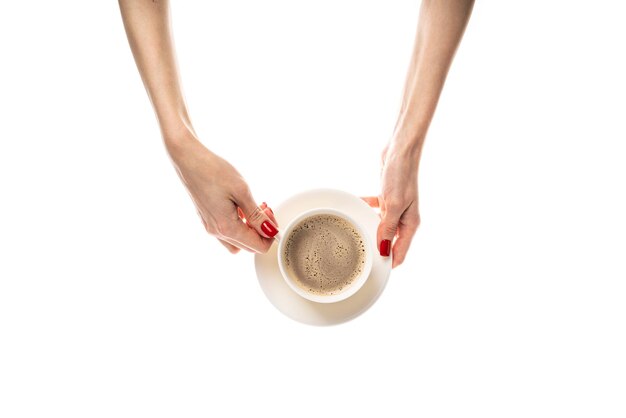 Le mani femminili tengono una tazza di ceramica bianca con un piattino su sfondo bianco Tazza di caffè con caffè latte cappuccino treinone caffè Mani femminili con manicure rossa fresca Isolato su sfondo bianco