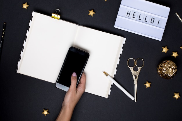 Le mani femminili utilizzano il telefono cellulare sul tavolo nero con dettagli in oro