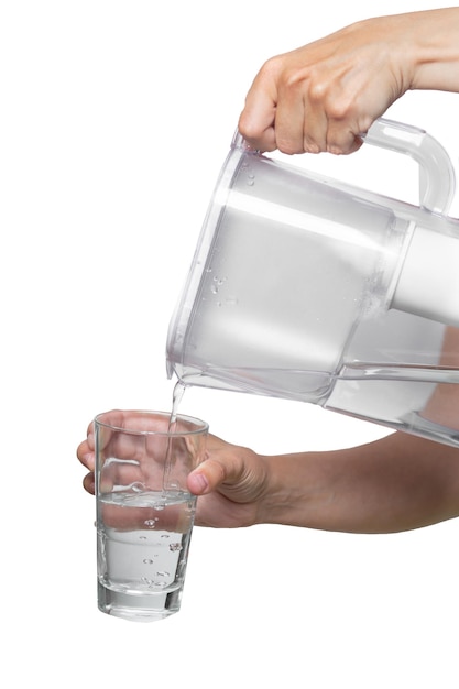 Le mani femminili versano acqua pulita da una caraffa filtrante in un bicchiere di vetro su sfondo bianco