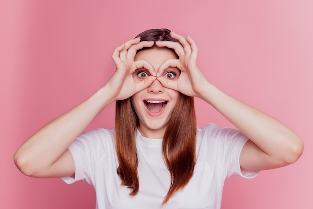 Le mani funky stupite sorprese della donna mostrano il binocolo sopra fondo rosa