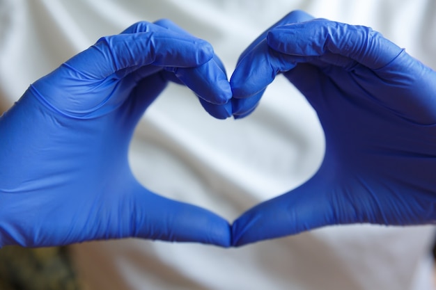 Le mani in guanti medici blu tengono le dita a forma di cuore. Gesti con le mani.