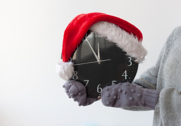 Le mani in guanti tengono l'orologio su cui è indossato il cappello di Babbo Natale