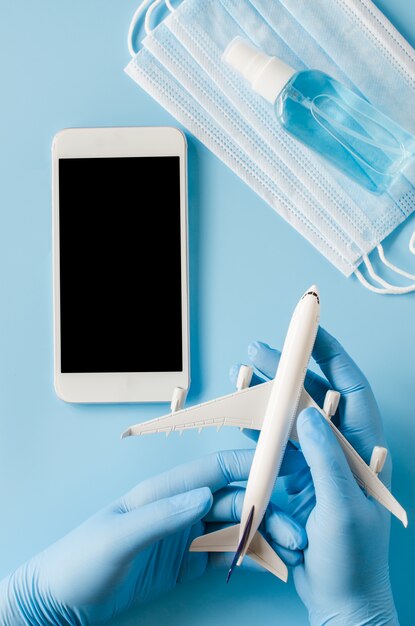 Le mani in guanti usa e getta tengono il modello dell'aeroplano con smartphone, maschera facciale e spray disinfettante per le mani