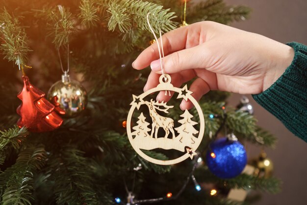 Le mani in maglione verde tengono e appendono cervi giocattolo di legno